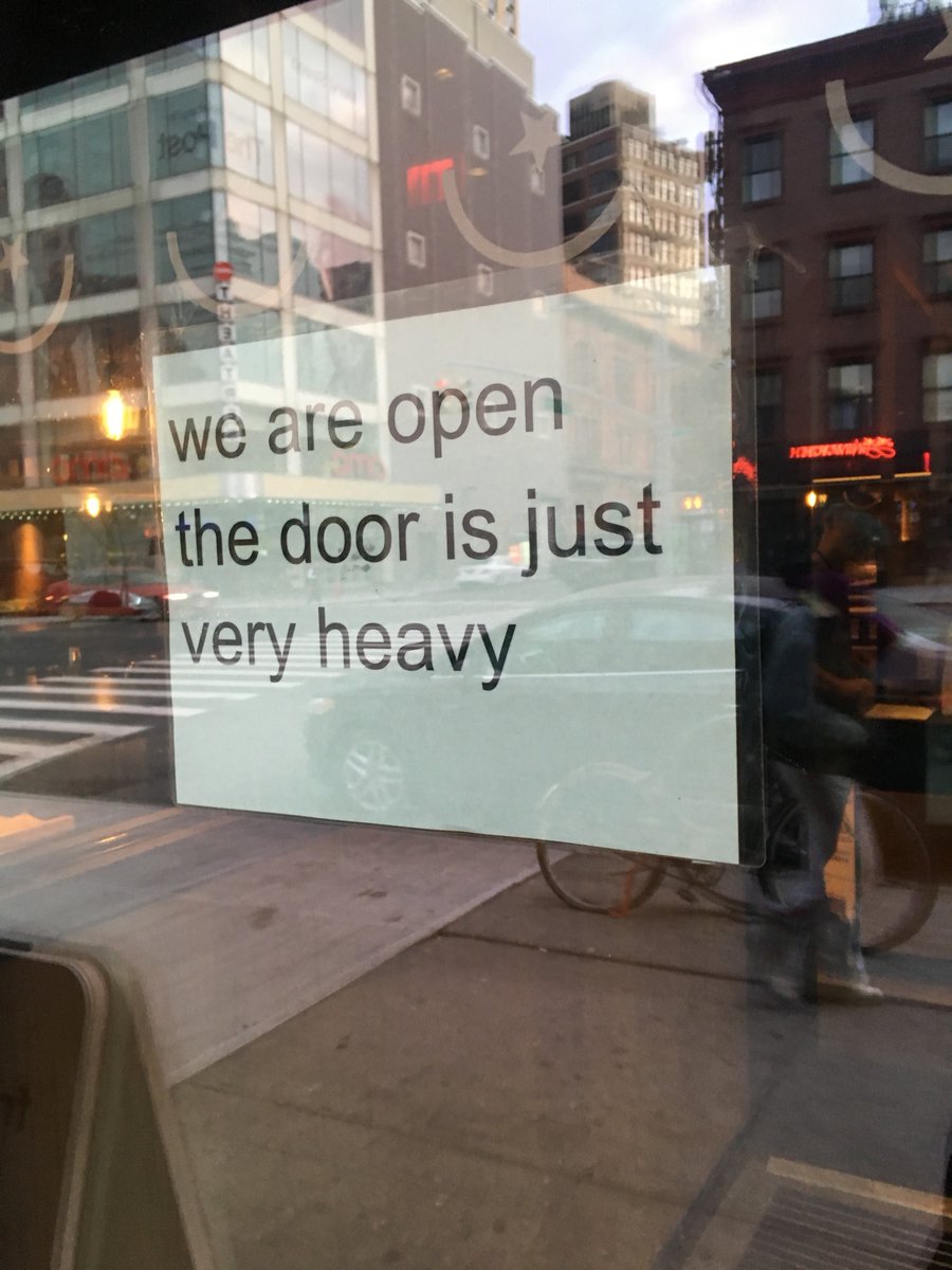 Photo of a storefront with a sign on the door that says 'we are open the door is just very heavy'